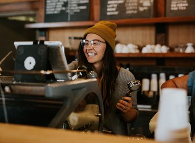 Person wearing glasses and a beanie using a coffee machine