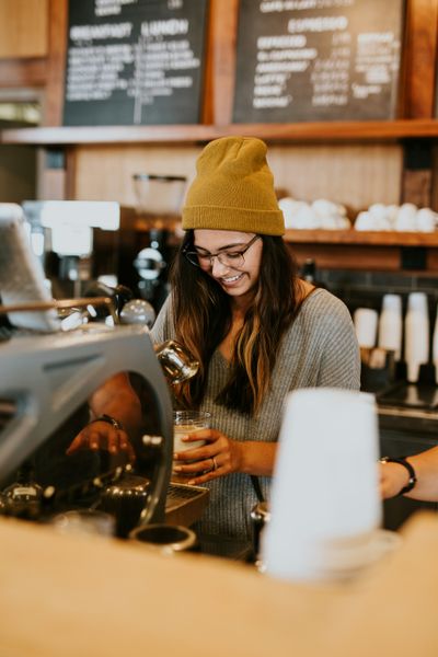 Person smiling and wearing glasses making a coffee